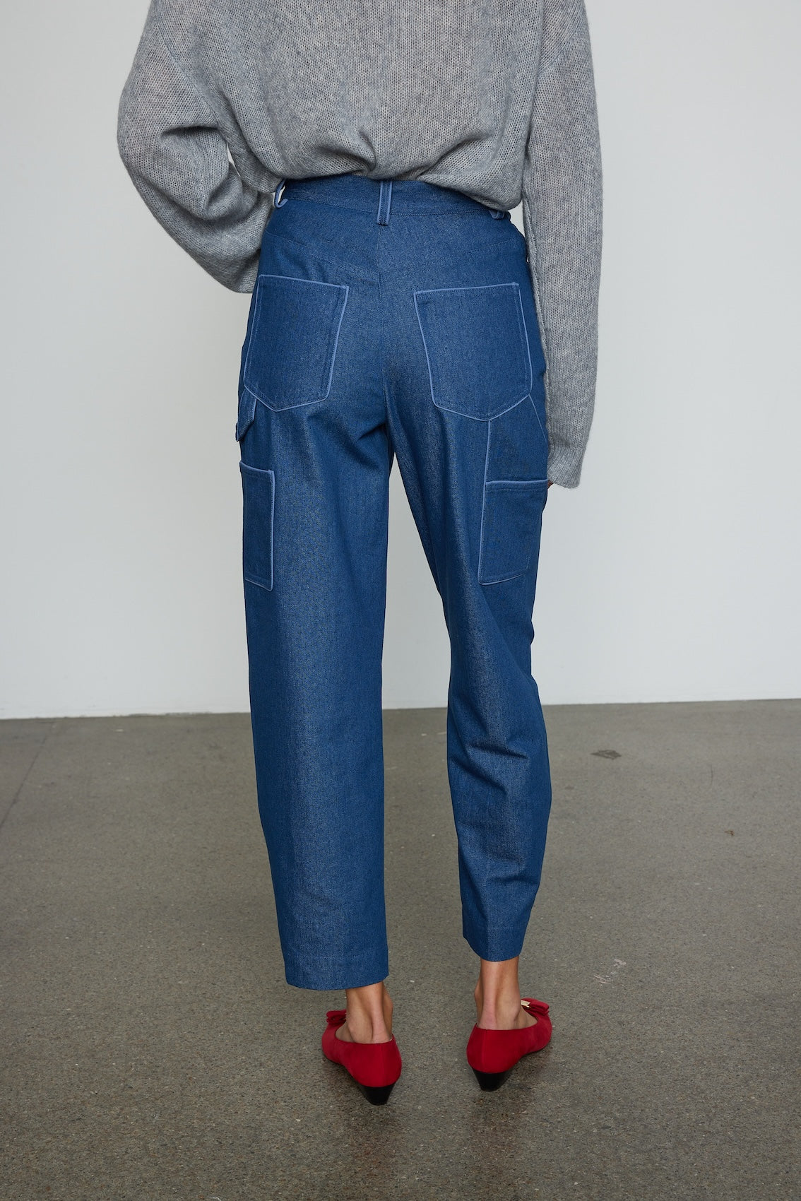 Caro Editions Emma Pants in Indigo Denim. The pants feature cargo details on the side and large pockets with piping details in a contrasting color. Easily modify the shape of the pants with a button adjustment. Style them with a t-shirt, blouse, or a matching Emma Jacket.