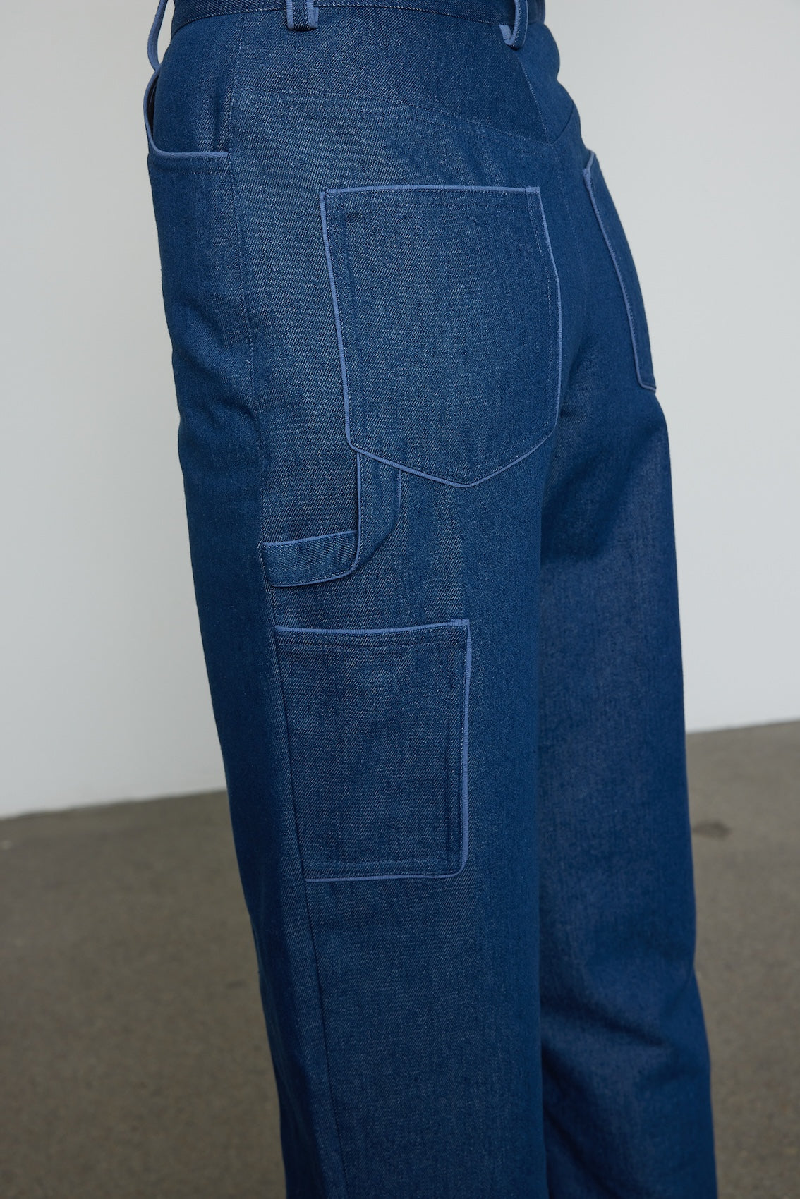 Caro Editions Emma Pants in Indigo Denim. The pants feature cargo details on the side and large pockets with piping details in a contrasting color. Easily modify the shape of the pants with a button adjustment. Style them with a t-shirt, blouse, or a matching Emma Jacket.